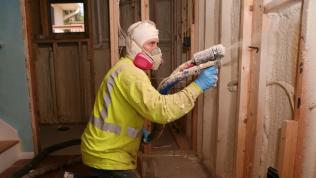 A person installing insulation into the wall of a house