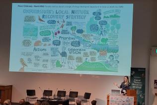 A woman stands in front of a projected slide displaying Oxfordshire's Local Nature Recovery Strategy
