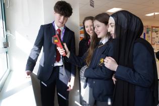 Three secondary school age children and a teacher use a thermal imaging camera on their classroom's windows.