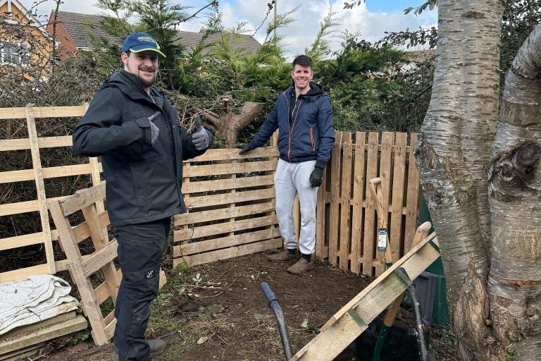 Two men smiling near a fence