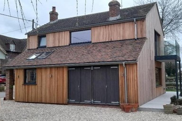A modern-looking, detached house, with modifications such as external wooden panels and double glazed windows.