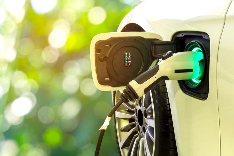 A close-up picture of a white EV car charging port with a charging cable plugged into it.
