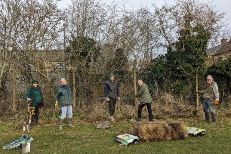 A group of 5 people planting hedges on a cloudy day.